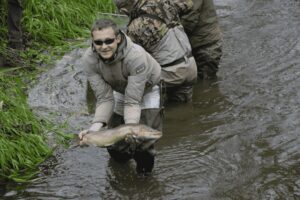 Angler practicing nymph fishing in a river, holding a freshly caught fish, showcasing effective fly fishing techniques.