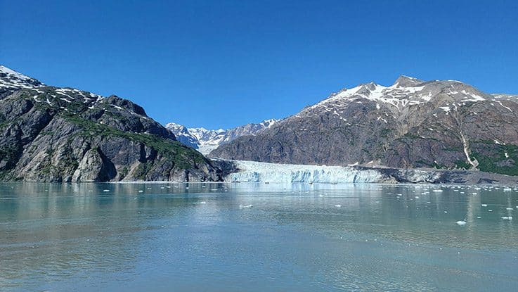 A breathtaking view of a glacial river surrounded by towering mountains in Alaska, a prime spot for adventurous fly fishing enthusiasts.